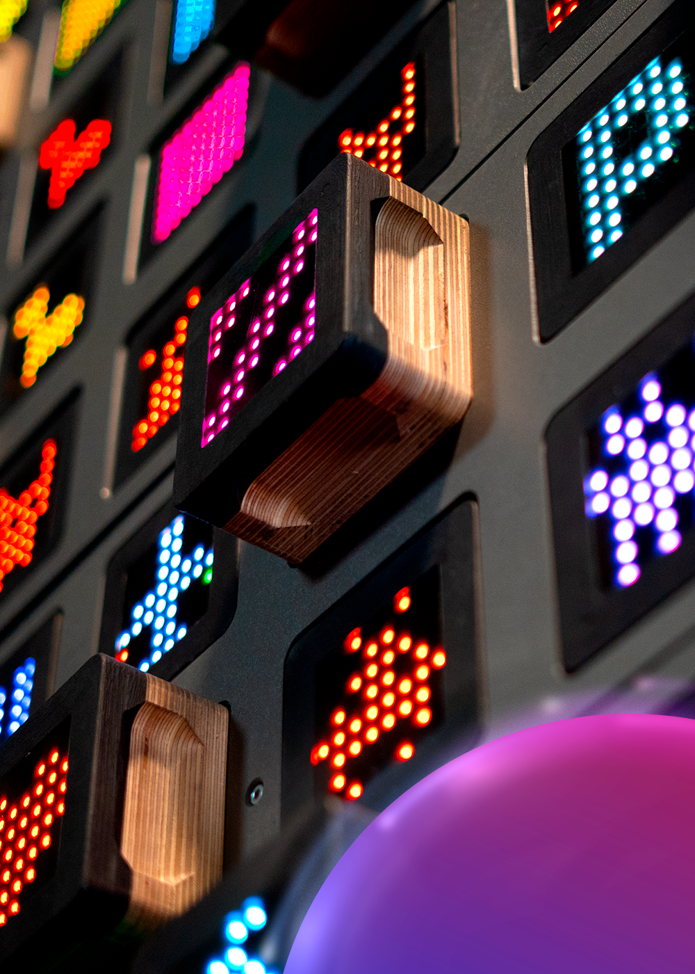 Pionowe ujęcie interaktywnej ścianki wspinaczkowej SkyWall z kolorowymi, pikselowymi ikonami LED i drewnianym chwytem na pierwszym planie.