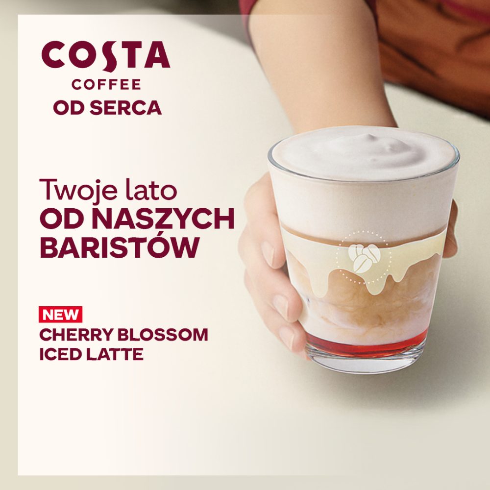 Grafika reklamowa Costa Coffee przedstawia dłoń trzymającą warstwową mrożoną kawę Cherry Blossom Iced Latte z czerwoną bazą i gęstą pianką. Obok szklanki widnieje logotyp marki oraz napisy promujące letnią ofertę baristów na jasnym, minimalistycznym tle.