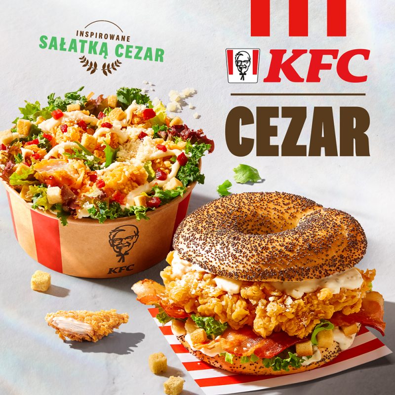 Reklama KFC prezentuje ofertę „Cezar”, w skład której wchodzi wypełniona warzywami i kurczakiem sałatka oraz bajgiel z panierowanym mięsem i dodatkami. Grafika utrzymana jest w jasnej kolorystyce z wyraźnymi elementami identyfikacji wizualnej sieci, takimi jak charakterystyczny czerwony logotyp.