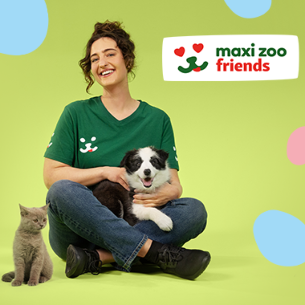 Grafika promocyjna Maxi Zoo Friends przedstawiająca uśmiechniętą kobietę siedzącą na zielonym tle z czarno-białym szczeniakiem na kolanach oraz szarym kotem obok. W prawym górnym rogu widoczne jest logo programu Maxi Zoo Friends.