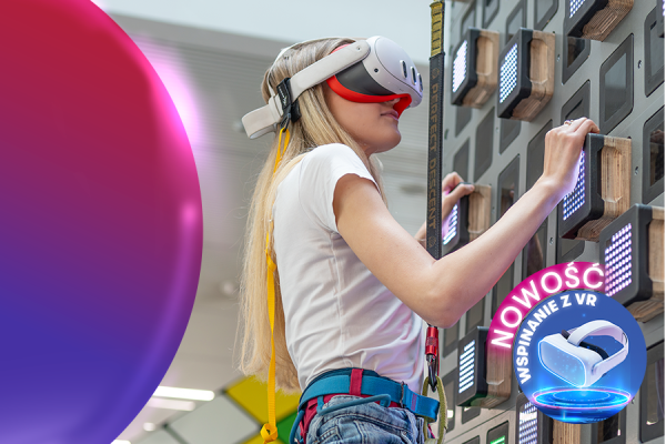 Dziewczynka w goglach VR wspina się po interaktywnej ściance wspinaczkowej z podświetlanymi chwytami podczas wydarzenia promującego wspinanie w wirtualnej rzeczywistości.