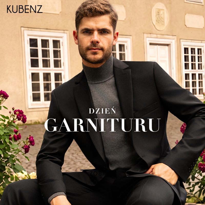 Grafika promocyjna marki Kubenz z okazji akcji „Dzień garnituru”. W lewym górnym rogu znajduje się czarne logo marki „KUBENZ”. Na zdjęciu plenerowym przed budynkiem w otoczeniu krzewów z różowymi różami siedzi elegancki mężczyzna z zarostem, ubrany w czarny garnitur, ciemnoszary golf oraz dopasowane spodnie. W centralnej części umieszczono biały napis „DZIEŃ GARNITURU”.