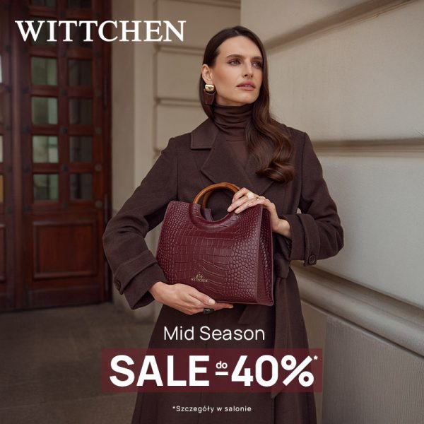 Elegancka kobieta w długim brązowym płaszczu i złotych kolczykach, trzymająca kuferek w kolorze wina z tłoczonej skóry z okrągłymi drewnianymi uchwytami
